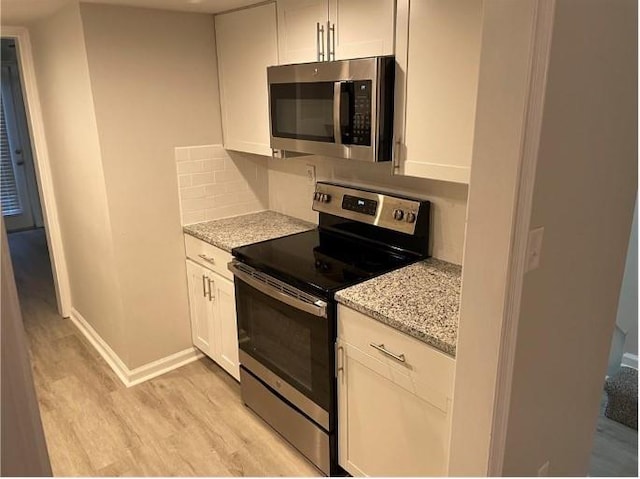 kitchen featuring light hardwood / wood-style flooring, appliances with stainless steel finishes, white cabinets, light stone counters, and backsplash