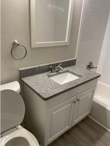 full bathroom featuring wood-type flooring, shower / bath combination, vanity, and toilet