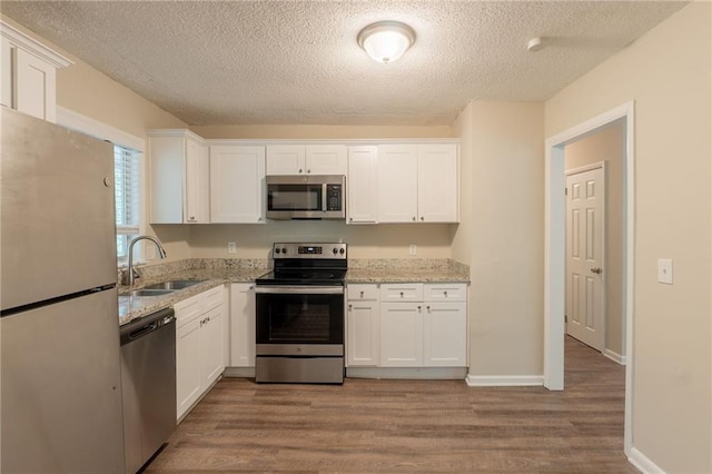 4669 Birch Ridge Trl, Stone Mountain, GA 30083 - kitchen with appliances with stainless steel finishes, a sink, a textured ceiling, white cabinets, and wood finished floors