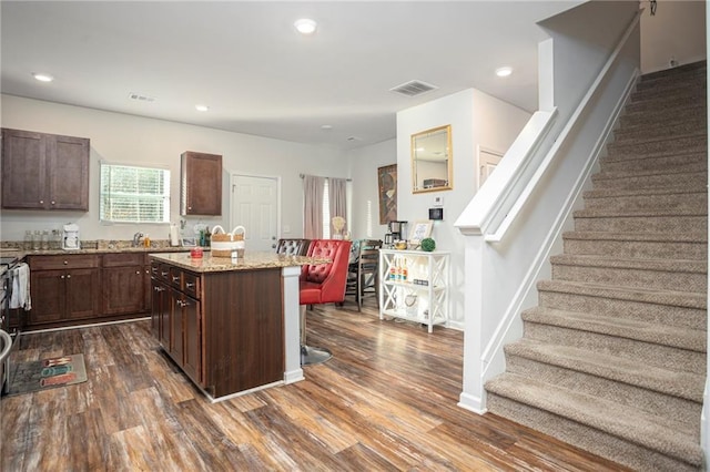 kitchen featuring light stone countertops, dark wood-type flooring, dark brown cabinetry, and a center island