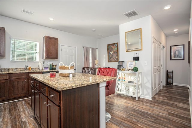 kitchen featuring light stone countertops, dark hardwood / wood-style flooring, a kitchen island, and dark brown cabinetry