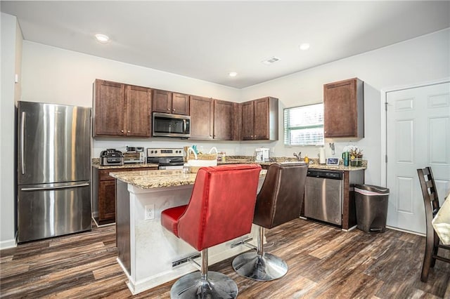 kitchen with dark wood-type flooring, appliances with stainless steel finishes, a kitchen breakfast bar, and a center island