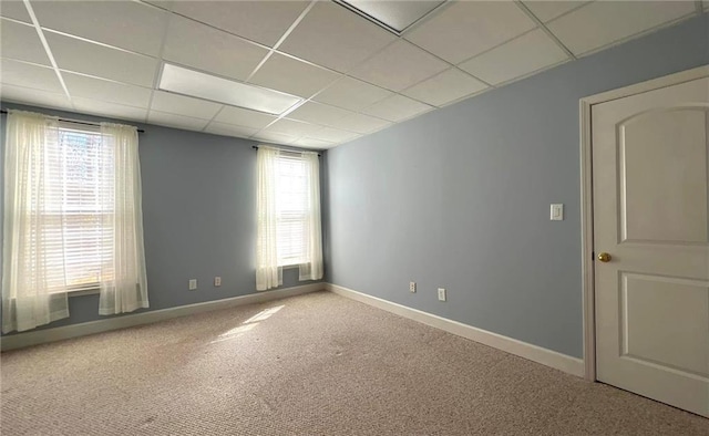 carpeted empty room featuring a paneled ceiling and baseboards