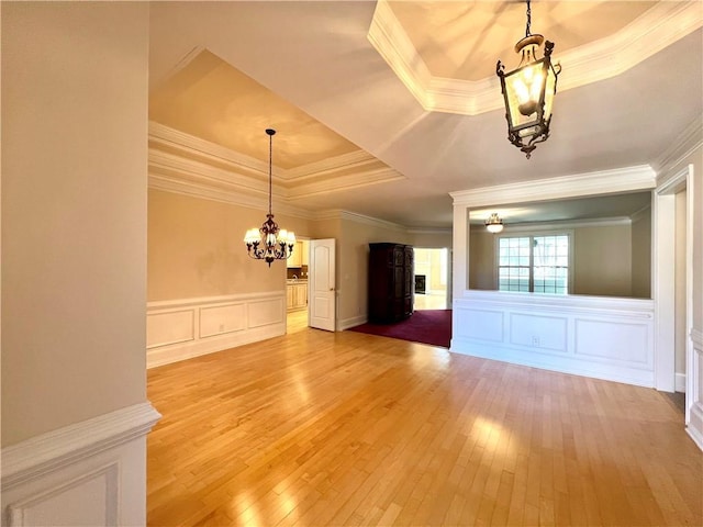 interior space with light wood finished floors, a tray ceiling, a decorative wall, and an inviting chandelier