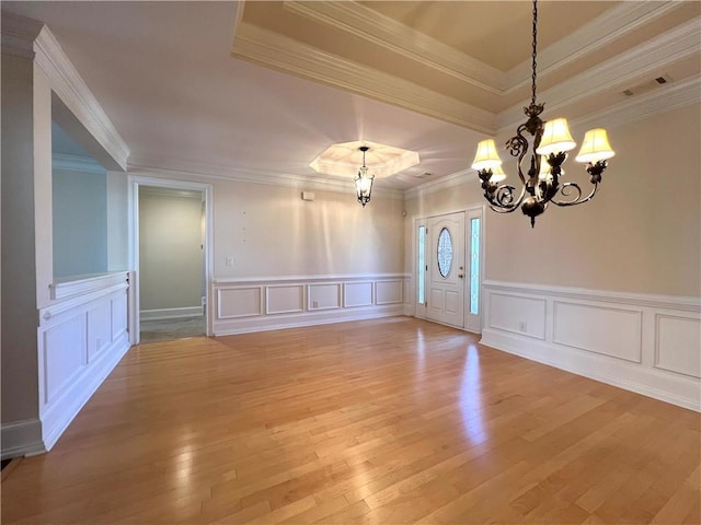 empty room featuring a tray ceiling, crown molding, a notable chandelier, visible vents, and light wood-type flooring