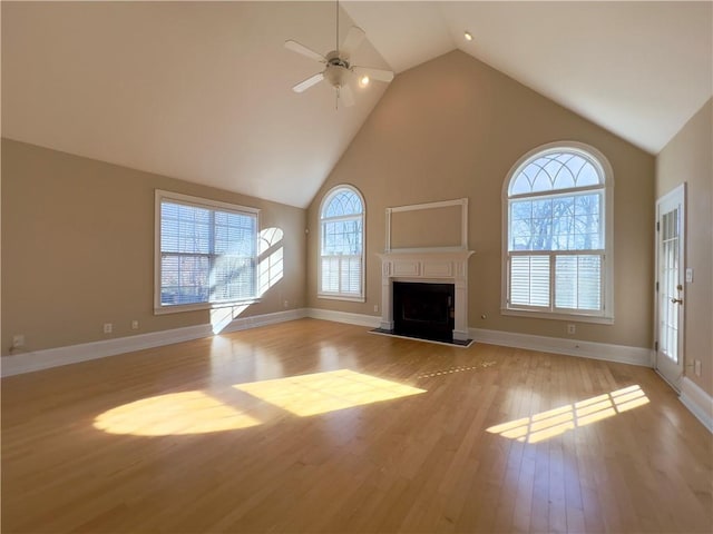 unfurnished living room featuring a fireplace with raised hearth, high vaulted ceiling, a wealth of natural light, and light wood-style floors