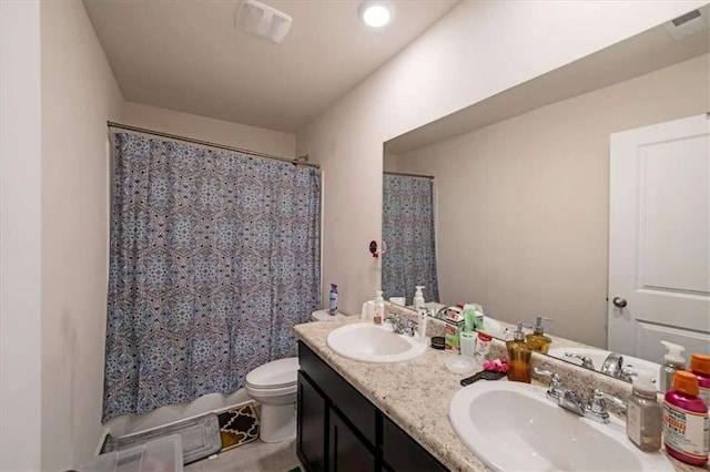 bathroom featuring visible vents, toilet, double vanity, and a sink