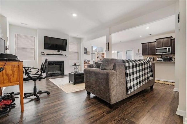 living room with dark wood-style flooring, a glass covered fireplace, recessed lighting, and baseboards