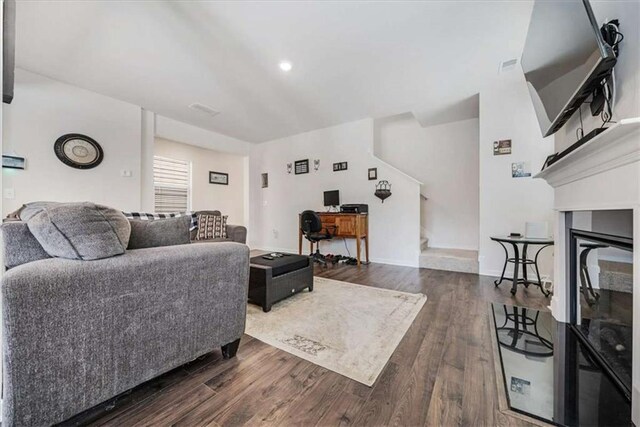 living area featuring stairway, a glass covered fireplace, baseboards, visible vents, and dark wood-type flooring