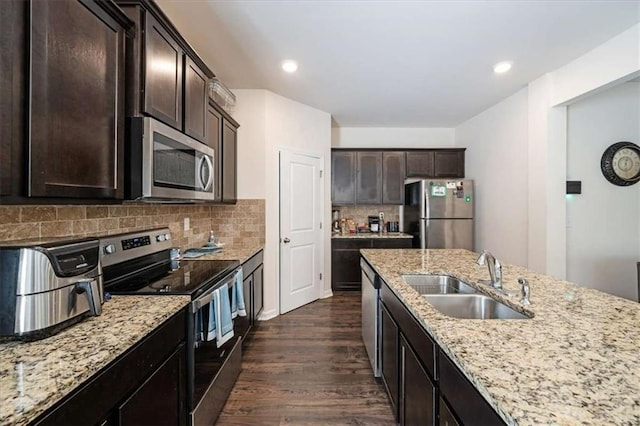 kitchen featuring a sink, appliances with stainless steel finishes, dark brown cabinets, dark wood-style flooring, and light stone countertops