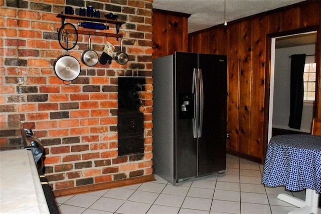 kitchen with a textured ceiling, light tile patterned floors, black fridge, and wooden walls