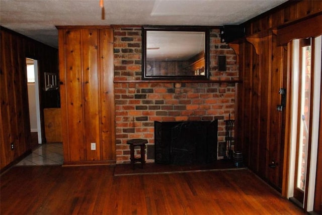 unfurnished living room featuring a fireplace, wood walls, a textured ceiling, and hardwood / wood-style floors