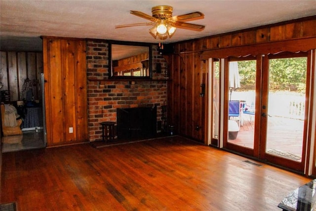 unfurnished living room with hardwood / wood-style floors, wooden walls, ceiling fan, a fireplace, and a textured ceiling