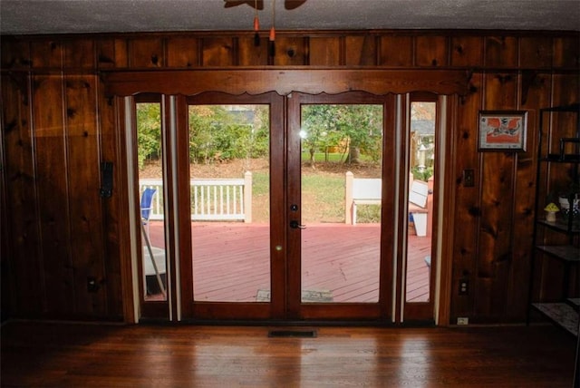 doorway with a textured ceiling, dark hardwood / wood-style floors, wood walls, and ceiling fan