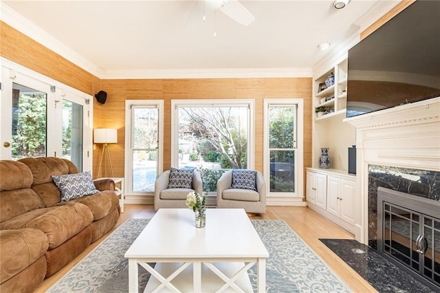 living room featuring ceiling fan, light wood finished floors, a premium fireplace, and crown molding