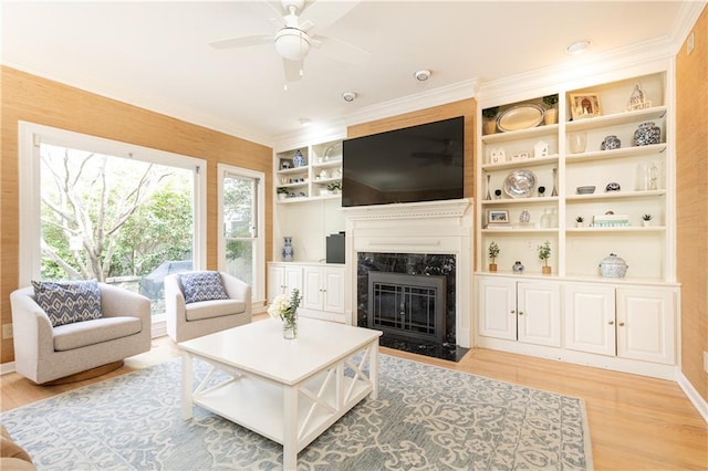 living room featuring ornamental molding, light wood-type flooring, a fireplace, and ceiling fan