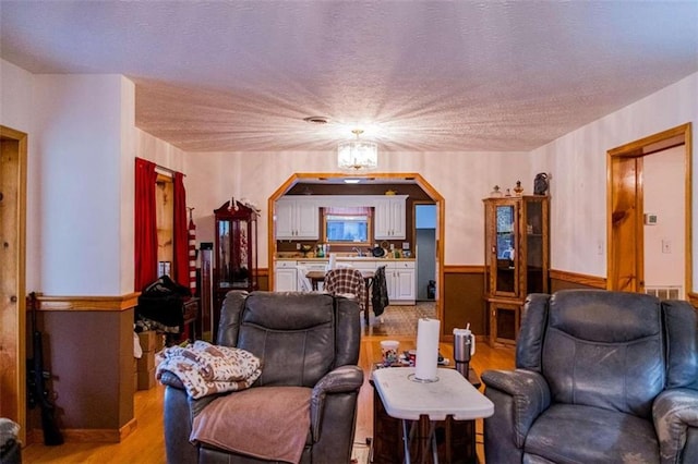 living room featuring a textured ceiling, light hardwood / wood-style floors, and a notable chandelier