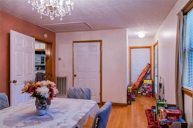 dining room with light hardwood / wood-style floors, a textured ceiling, and a notable chandelier