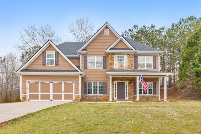 craftsman-style house featuring driveway, an attached garage, a shingled roof, a front lawn, and stone siding