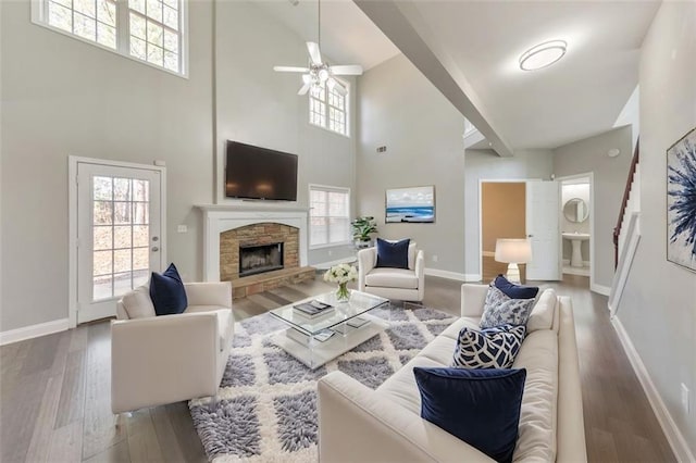 living room featuring baseboards, a ceiling fan, stairway, wood finished floors, and a stone fireplace