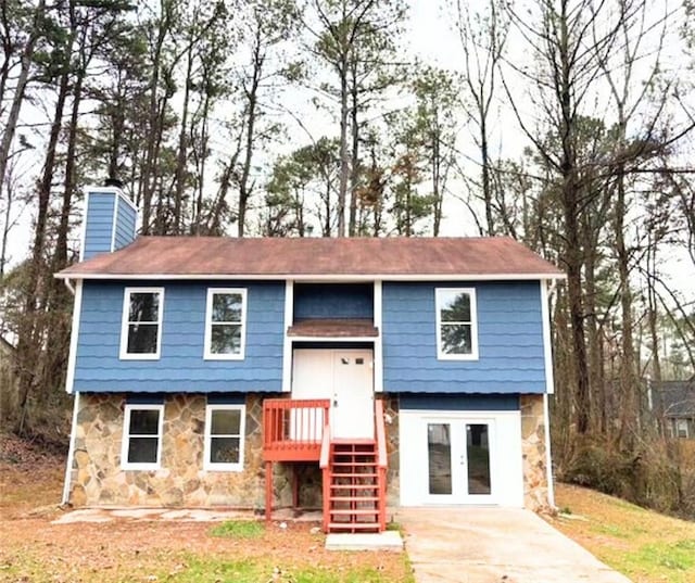 bi-level home with stone siding, a chimney, and french doors