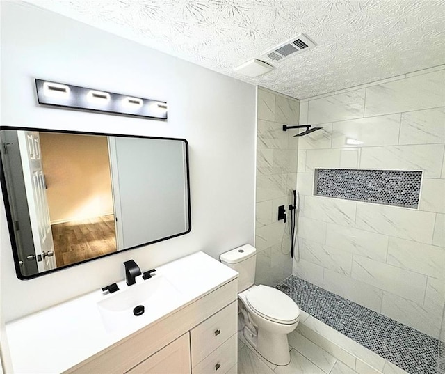 bathroom featuring vanity, a textured ceiling, toilet, and tiled shower