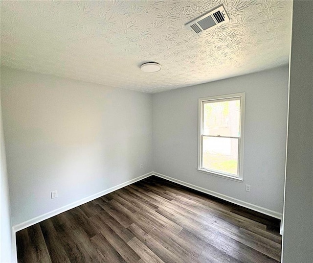 empty room with dark hardwood / wood-style floors and a textured ceiling