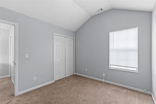 unfurnished bedroom with light carpet, a closet, and lofted ceiling