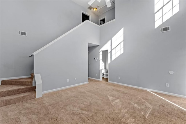 unfurnished living room featuring carpet flooring, a high ceiling, and ceiling fan