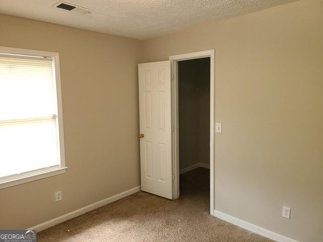 carpeted empty room with baseboards, visible vents, and a textured ceiling
