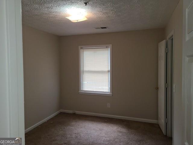 unfurnished room featuring baseboards, visible vents, carpet, and a textured ceiling