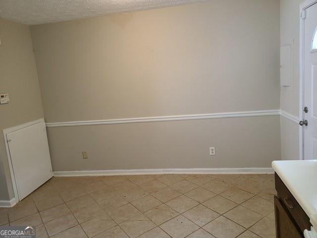 interior space featuring a textured ceiling, baseboards, and light tile patterned floors