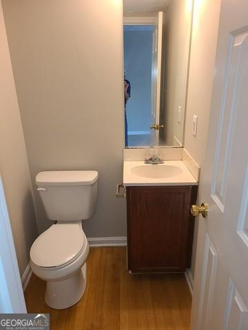 half bathroom with toilet, vanity, wood finished floors, and baseboards