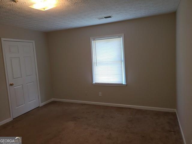 carpeted spare room with baseboards, visible vents, and a textured ceiling