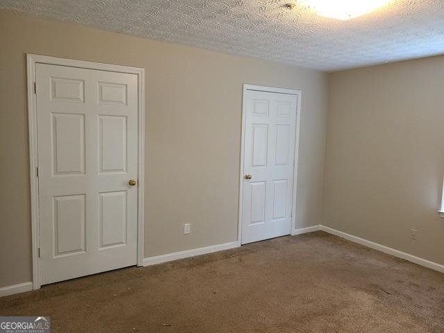 unfurnished bedroom featuring carpet floors, a textured ceiling, and baseboards