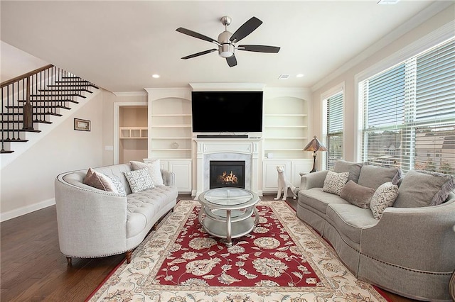 living room with wood finished floors, a ceiling fan, baseboards, stairs, and ornamental molding