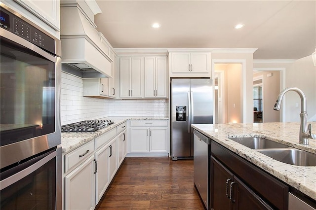 kitchen with white cabinets, custom range hood, dark wood-type flooring, stainless steel appliances, and a sink