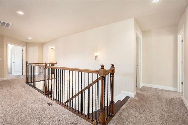 corridor featuring carpet floors, baseboards, visible vents, and an upstairs landing