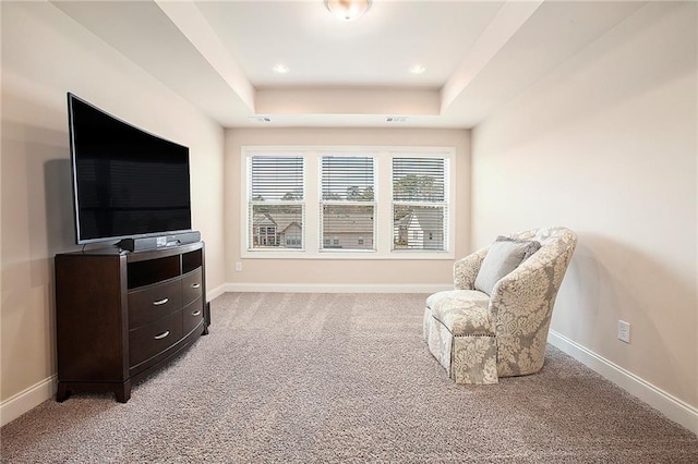 living area with a tray ceiling, light carpet, and baseboards