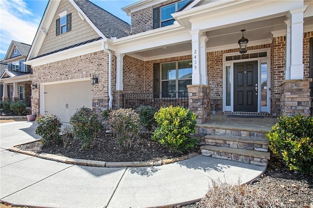 entrance to property featuring covered porch, driveway, brick siding, and a garage