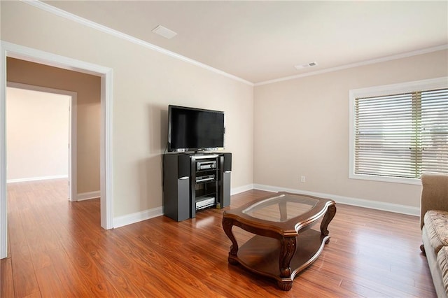 living area featuring baseboards, visible vents, ornamental molding, and wood finished floors