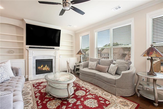 living area featuring visible vents, built in features, ornamental molding, wood finished floors, and a fireplace