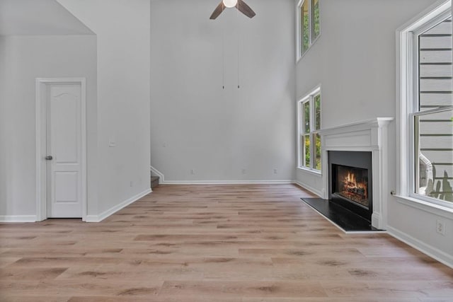2934 Mill Grove Ter, Dacula, GA 30019 - unfurnished living room with a warm lit fireplace, ceiling fan, light wood finished floors, stairs, and a high ceiling