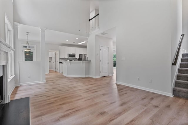 2934 Mill Grove Ter, Dacula, GA 30019 - unfurnished living room featuring stairs, light wood-type flooring, a fireplace with flush hearth, and a high ceiling