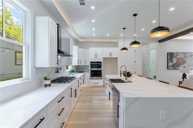 kitchen with stainless steel appliances, a sink, white cabinetry, a center island with sink, and light wood-style floors