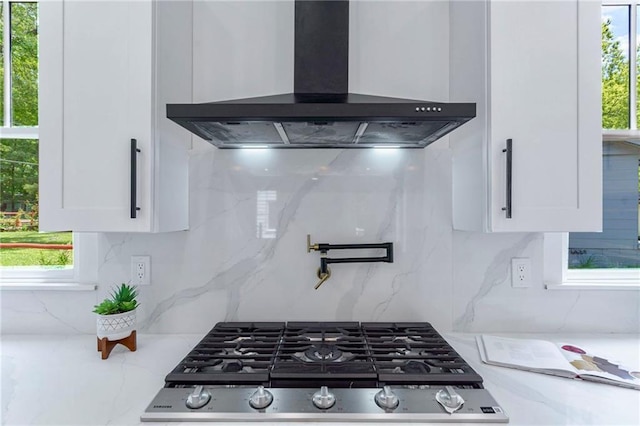 kitchen view of wall chimney exhaust hood, pot filler, white cabinets, and backsplash