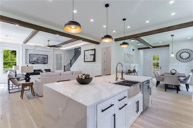 kitchen featuring a sink, a decorative wall, stainless steel dishwasher, light wood finished floors, and beam ceiling