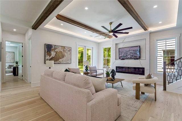 living area featuring stairway, a ceiling fan, a fireplace, beam ceiling, and light wood-style flooring
