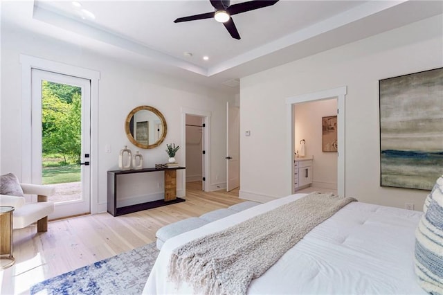 bedroom featuring access to exterior, light wood finished floors, a raised ceiling, baseboards, and connected bathroom
