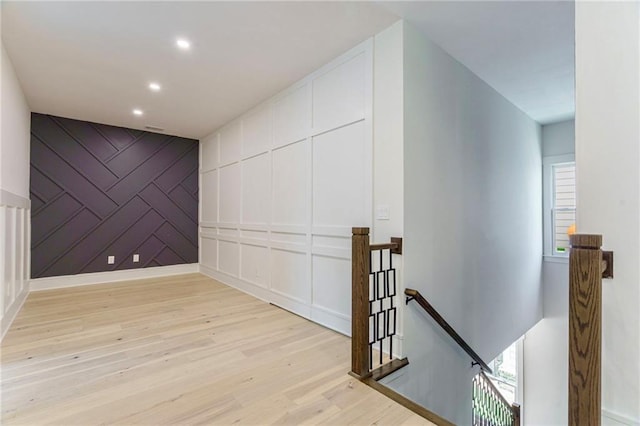 hall with an upstairs landing, light wood-style floors, recessed lighting, a decorative wall, and an accent wall